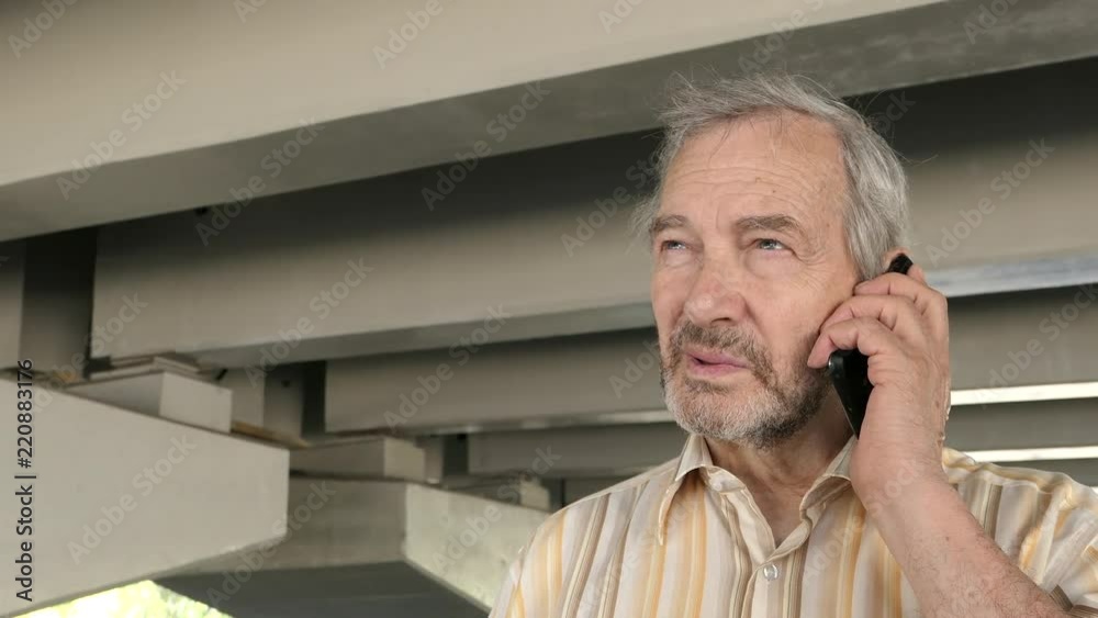 An Elderly Man Standing Under The Overpass And Talking On A Mobile Phone