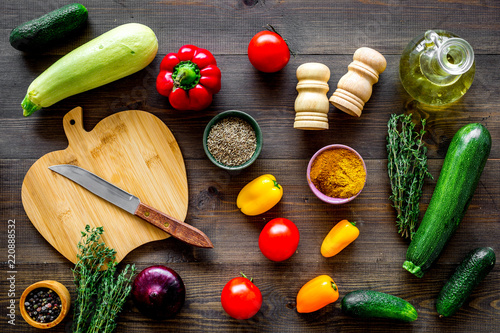 Cooking vegetable stew concept. Fresh vegetables squash, bell pepper, tomato, spices and cutting doard on dark wooden background top view photo