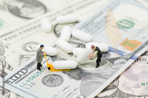 Healthcare, medical or pharmaceutical industry business concept, miniature worker using forklift to manage or move white tablet pills on US dollar money banknotes
