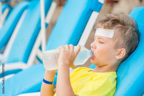 Little boy on the beach with a sunstroke drink water