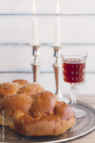 Shabbat or Sabbath kiddush ceremony composition with a traditional sweet fresh loaf of challah bread, glass of red kosher wine and candles on a vintage wood background