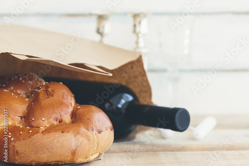 Shabbat or Sabbath grocery shopping composition with a traditional sweet fresh loaf of challah bread with a bottle of red kosher wine on a vintage wood background