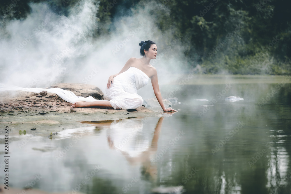Asian woman in a white bathrobe, enjoying touching water in a stream in the nature.