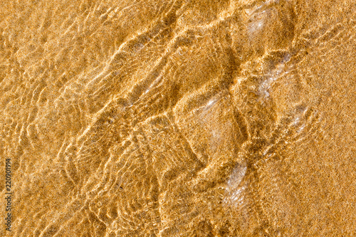 Golden sand under transparent sea water, abstraction, texture, background of sand pattern on a beach in the summer closeup of sand under the water