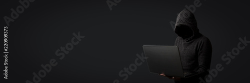 Faceless man in a hoodie with a hood holds a laptop in his hands