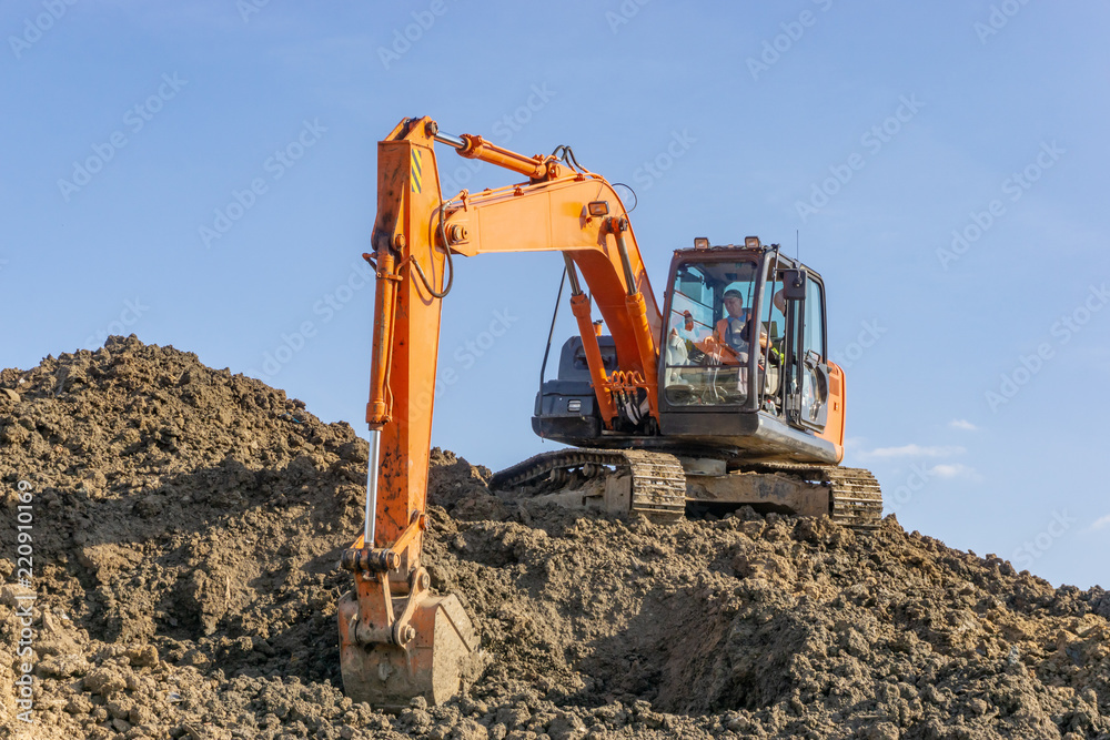 Orange excavator loads the land on a construction site.. Orange excavator loads the land on a construction site..