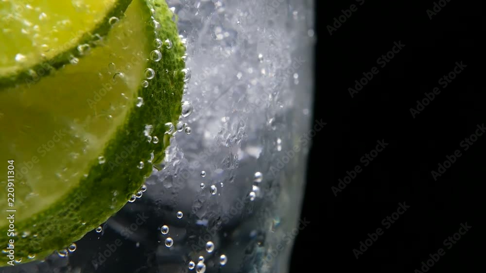 Macro close-up,refreshing soda tonic fizzy water, lime in Glass, ice. Slice of lemon, mineral bubbles. Detox or thirst concept. Healthy, dietary nutrition. Cold lemonade mojito drink. Black background
