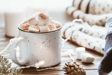 Hot cocoa with marshmallow in a white ceramic mug surrounded by winter things on a wooden table. The concept of cosy holidays and New Year.