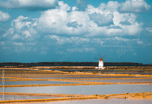 A white lighthouse with a red roof in the middle of the salt marshes of Marsala in Sicily, Italy, on a beautiful sunny day with a blue sky reflecting on the water