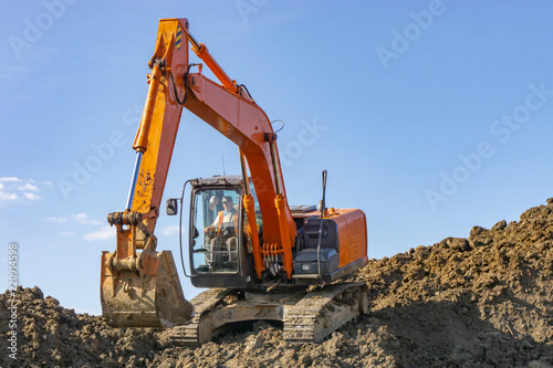 Orange excavator loads the land on a construction site..
