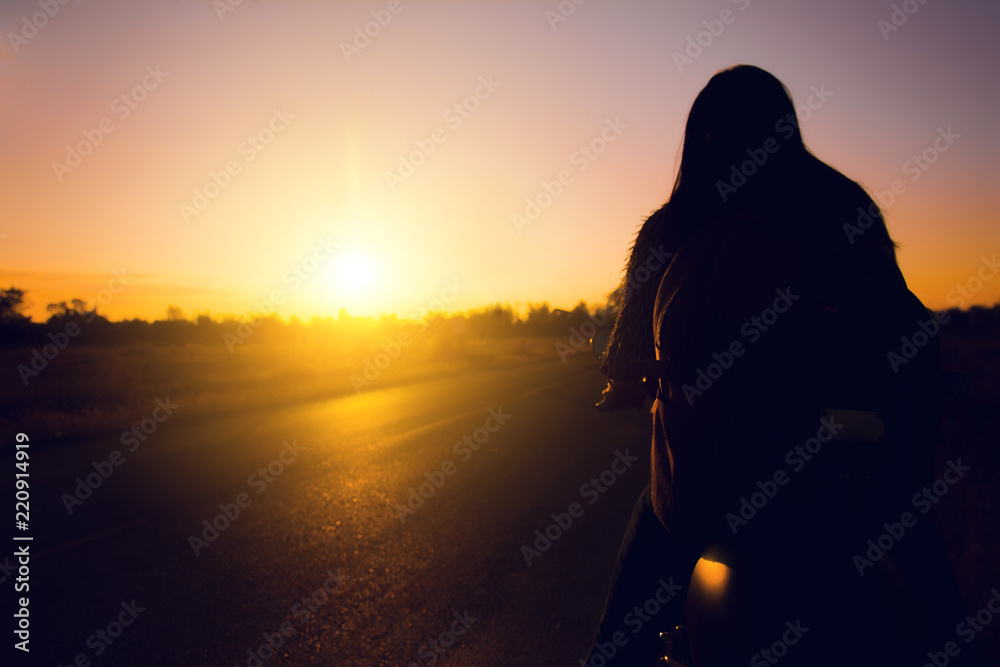 Silhouette of biker woman  with his motorbike(motorcycle ) on street,he shoulder backpack, enjoying freedom and active lifestyle, having fun on a bikers tour sunset background.