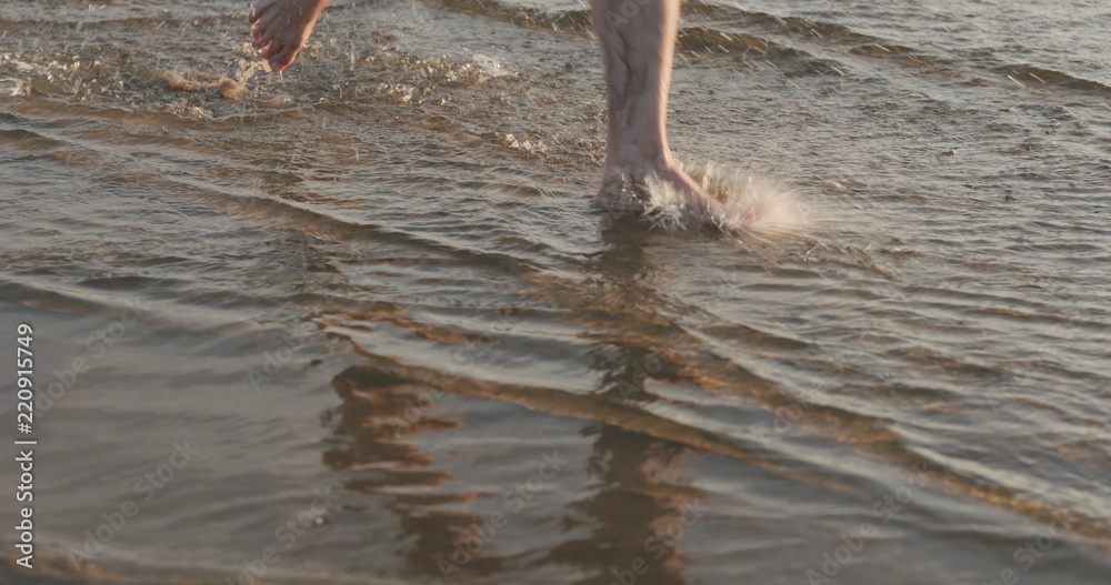 closeup of man legs running in shallow water on a beach on sunny day