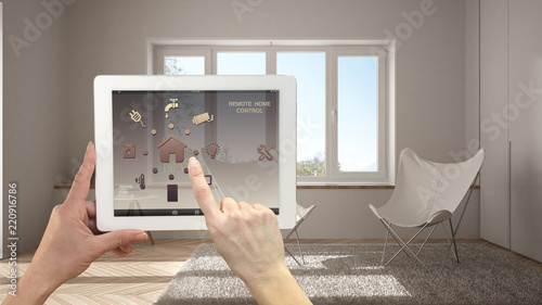 Smart remote home control system on a digital tablet. Device with app icons. Minimalist modern bright living room in the background, architecture interior design
