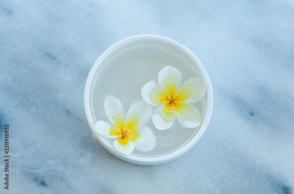 Top view of tropical flower in white bowl with water on white table Top view of tropical flower in white bowl with water on white table