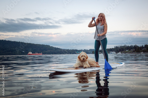 Girl with a dog on a paddle board during a vibrant summer sunset. Taken in Deep Cove, North Vancouver, BC, Canada. photo