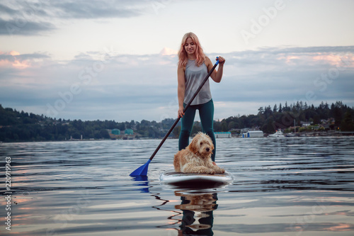 Girl with a dog on a paddle board during a vibrant summer sunset. Taken in Deep Cove, North Vancouver, BC, Canada.