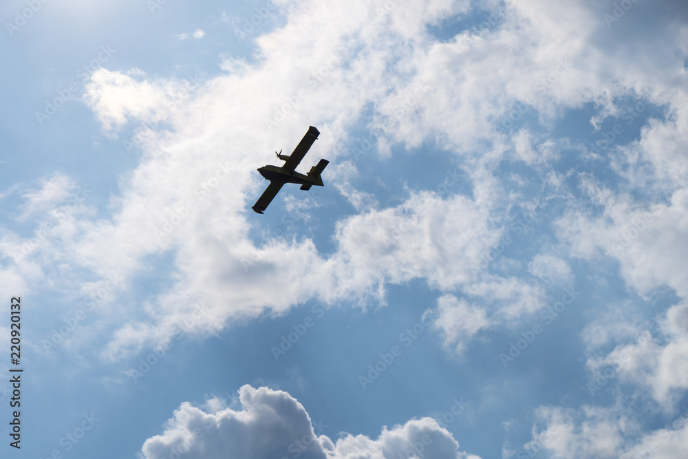 Canadair, a water bomber aircraft, silhouette on blue sky with clouds Canadair, a water bomber aircraft, silhouette on blue sky with clouds