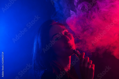 Portrait of young woman in neon red and blue smoke with vape or e-cigarettes
