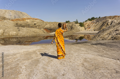 Fotografi a girl in a sari with a pitcher on her shoulder goes for water to a dirty lake i
