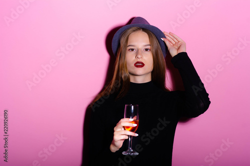 Aperol. Girl drinks alcohol. Aperitif. Girl with a bright makeup. Pink background. Style. Image. Blue hat