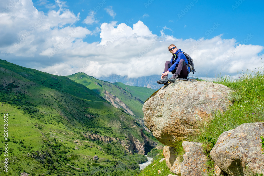A girl with a backpack is sitting on a rock. Mountain landscape. Mountain climbing in the Caucasus.