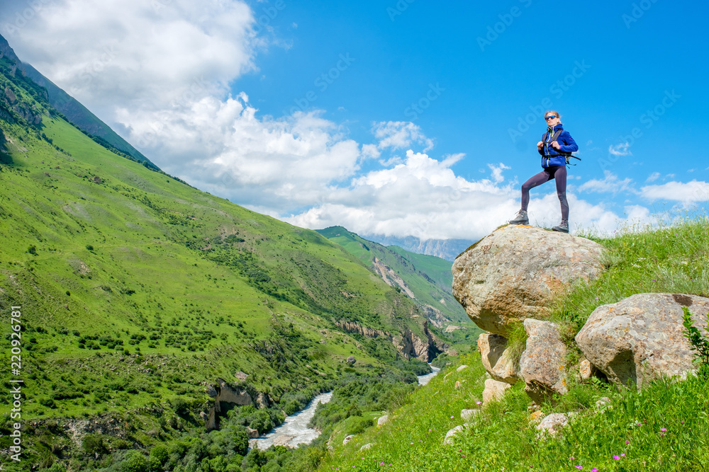 A girl with a backpack is standing on a rock. Mountain landscape. Mountain climbing in the Caucasus.