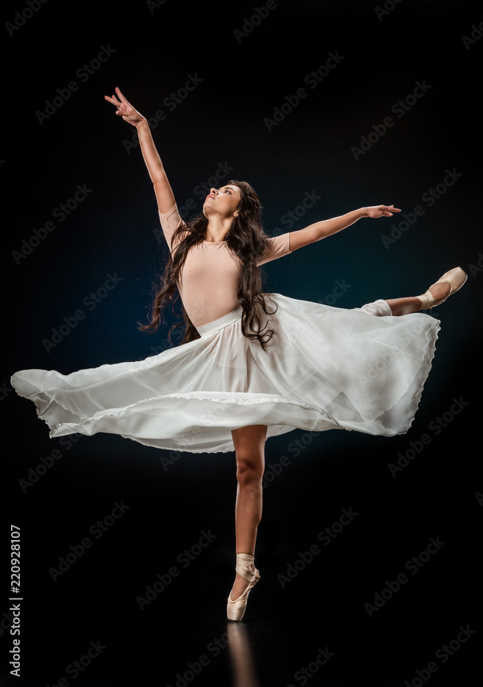 elegant female ballet dancer in white skirt dancing on dark background