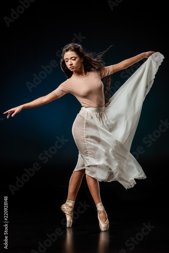 elegant female ballet dancer in white skirt dancing on dark background