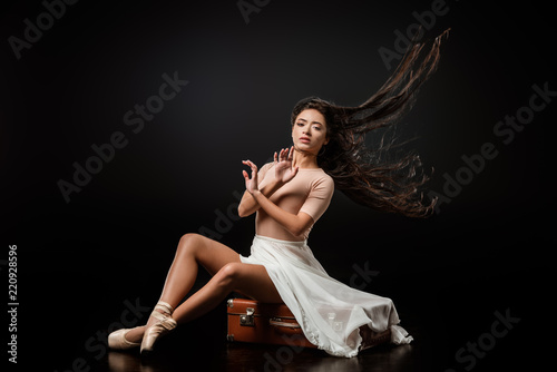 beautiful ballerina in white skirt resting on retro suitcase on dark background