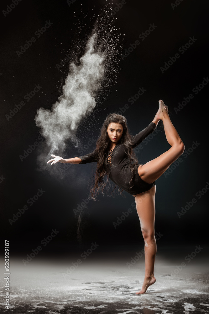 young ballerina in black bodysuit with talc powder dancing on dark background