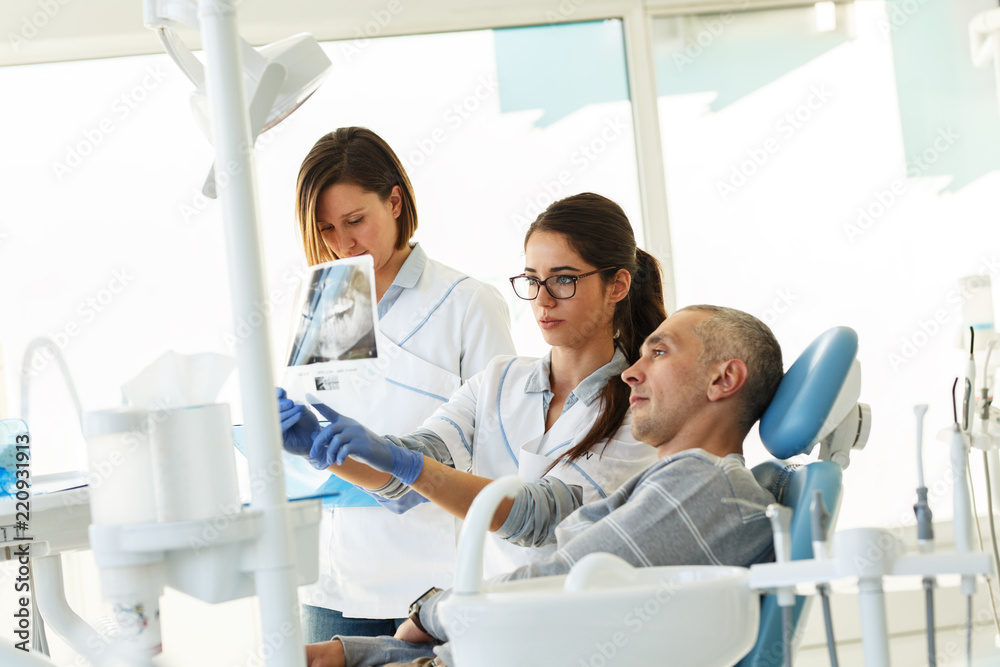 Dentist and his assistant in dental office talking with female patient and preparing for treatment.Examining x-ray image. Dentist and his assistant in dental office talking with female patient and preparing for treatment.Examining x-ray image.