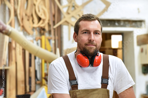 portrait of a carpenter in work clothes and hearing protection in the workshop of a carpenter's shop