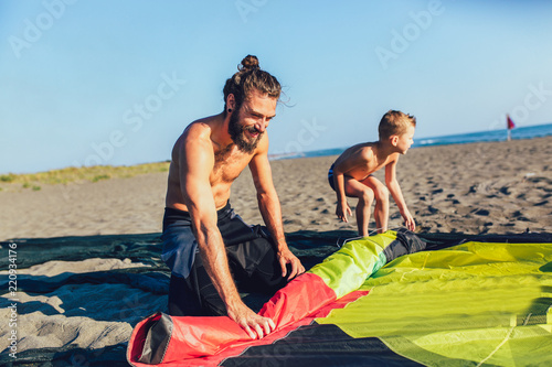 Man sufrers with his son in wetsuits with kite equipment for surfing.
