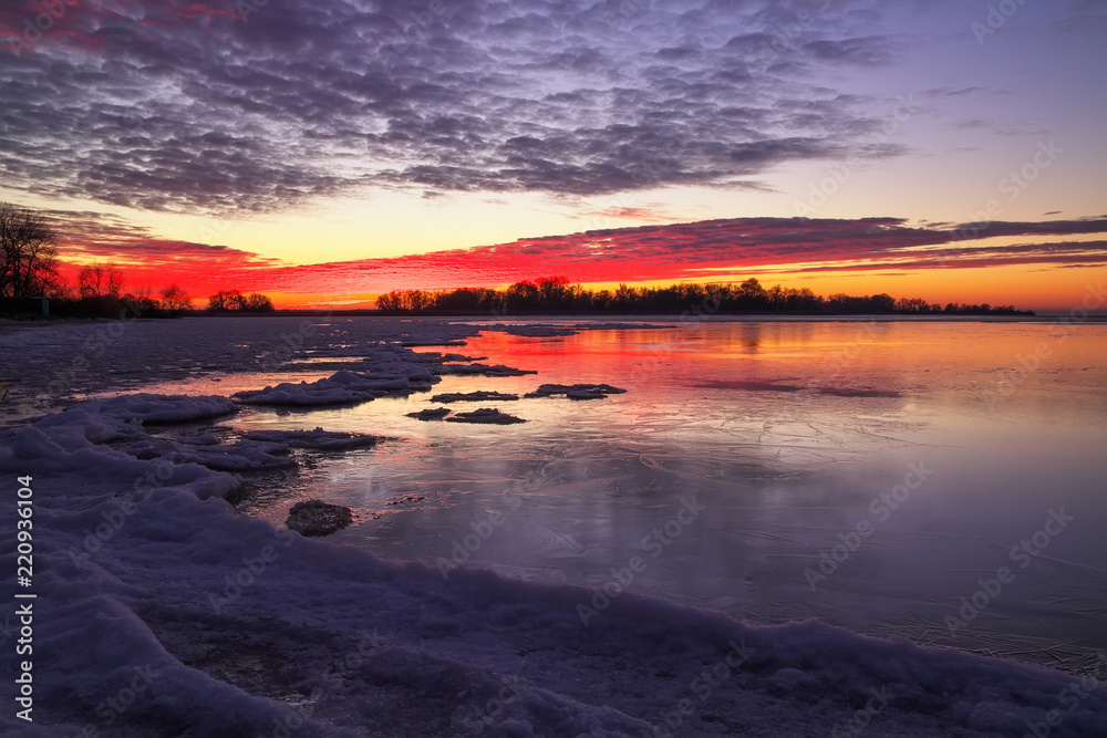 Beautiful colorful winter landscape with frozen lake and sunset sky. Unusual weather phenomenon