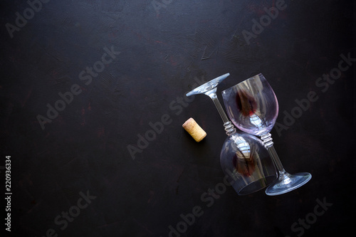 Two wineglasses with red wine, cork and grape leaves lying on dark wooden background. Top view. Flat lay. Copy space