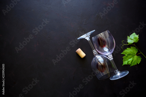 Two wineglasses with red wine, cork and grape leaves lying on dark wooden background. Top view. Flat lay. Copy space