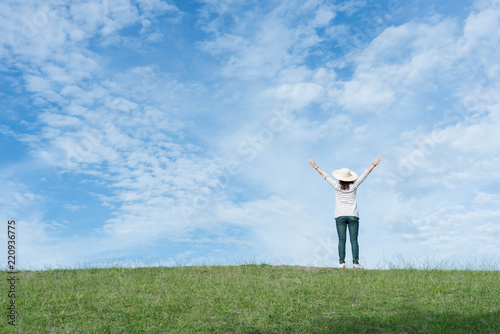 Standing woman raised her hands on the mountain, natural green and beautiful sky.