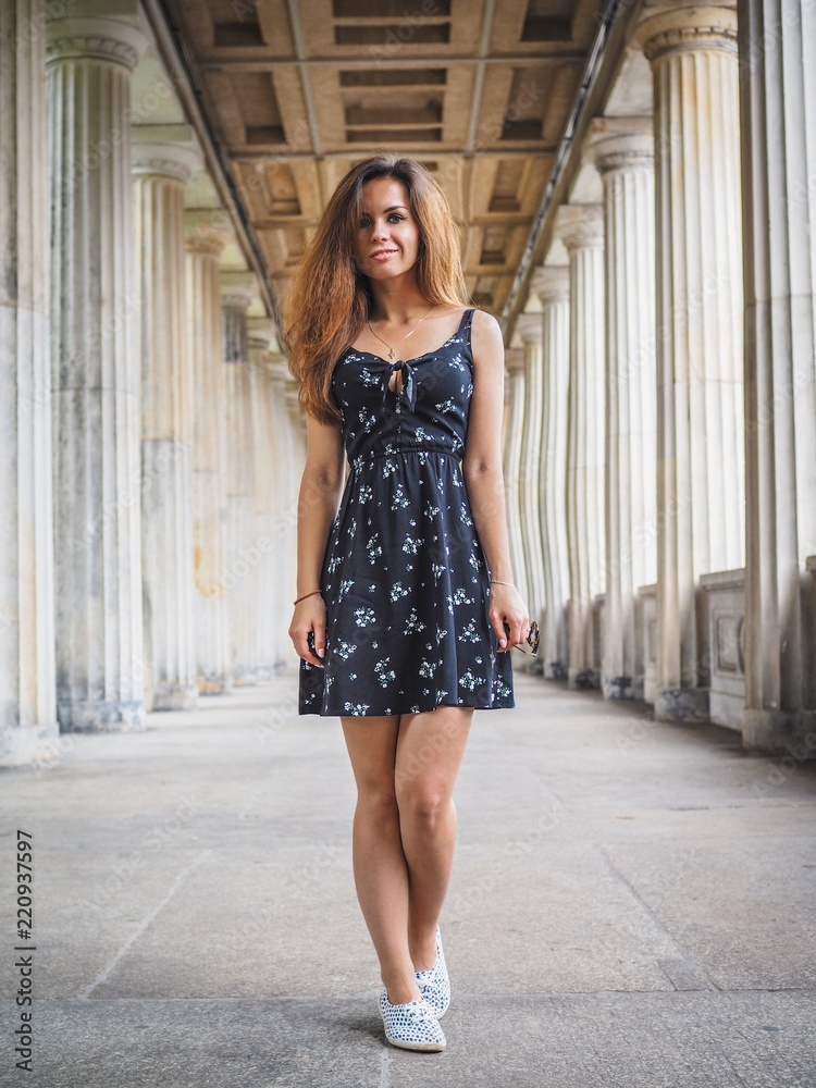 Brunette girl with long hair in black short dress stands between a long row  of columns Stock Photo | Adobe Stock