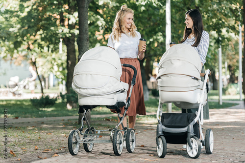 Konstfotografi mothers holding coffee to go and walking with baby strollers in park