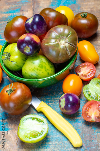 Multicolored assortment of French fresh ripe tomatoes in green bowl on blue wooden table