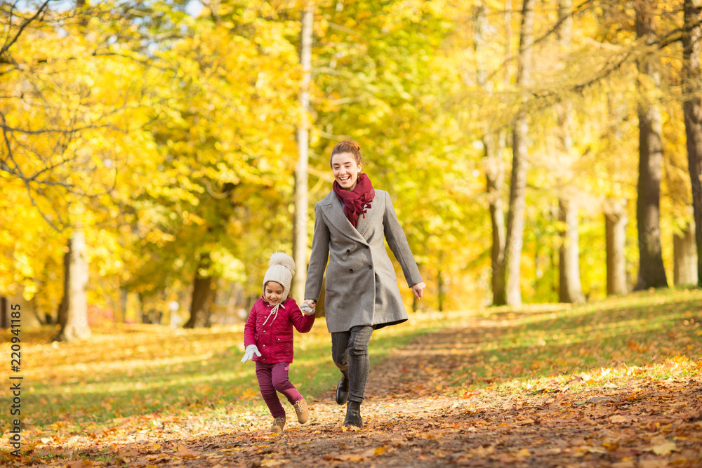 family, season and people concept - happy mother and little daughter walking along autumn park