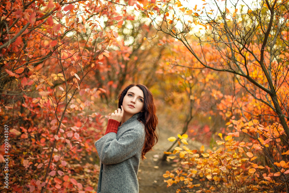 young beautiful woman in grey coat sweather walking in autumn park with yellow and red leaves