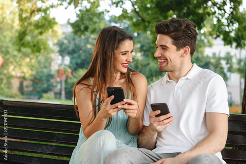 Loving couple sitting outdoors while using mobile phones.