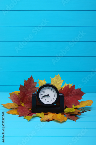 Autumn leafs and alarm clock on wooden background