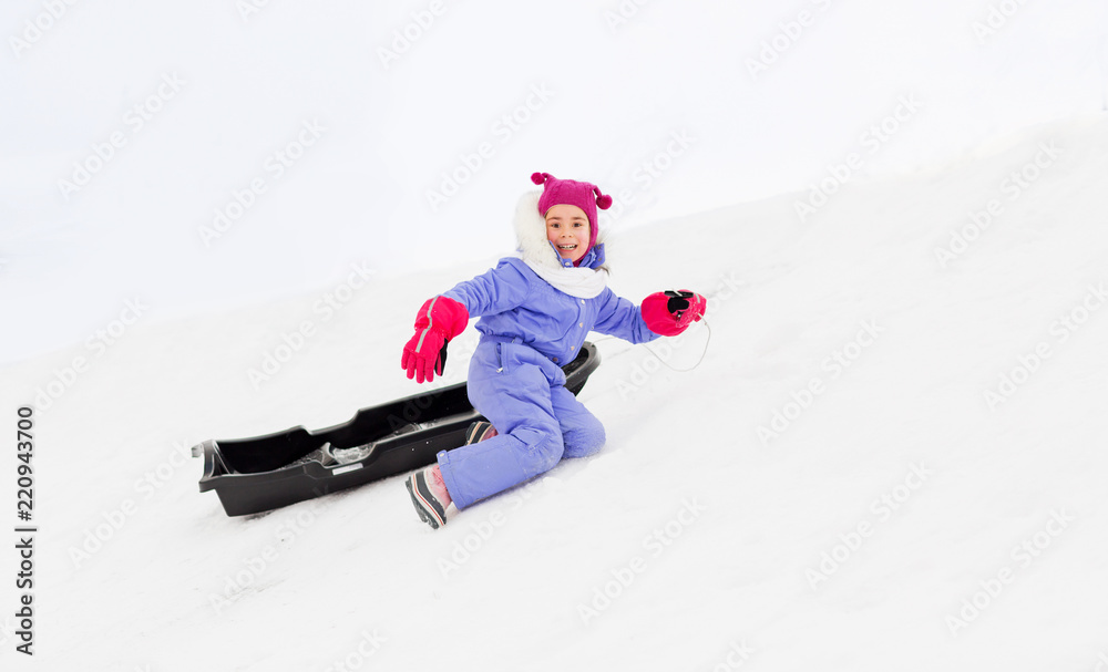 childhood, sledging and winter season concept - happy little girl with sled on snow hill
