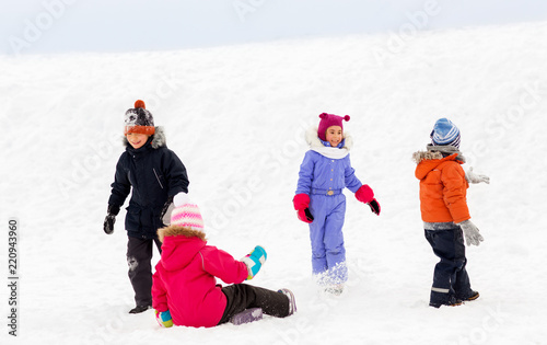 childhood, leisure and season concept - group of happy little kids in winter clothes playing outdoors