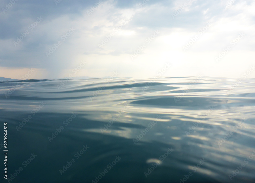 Background texture of clear, blue sea at water level and a cloudy evening sky