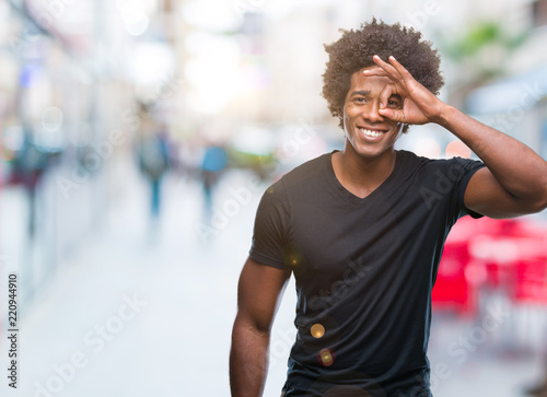 Afro american man over isolated background doing ok gesture with hand smiling, eye looking through fingers with happy face. © Krakenimages.com