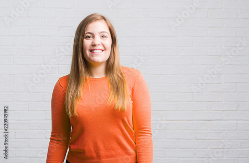 Young adult woman over white brick wall with a happy face standing and smiling with a confident smile showing teeth