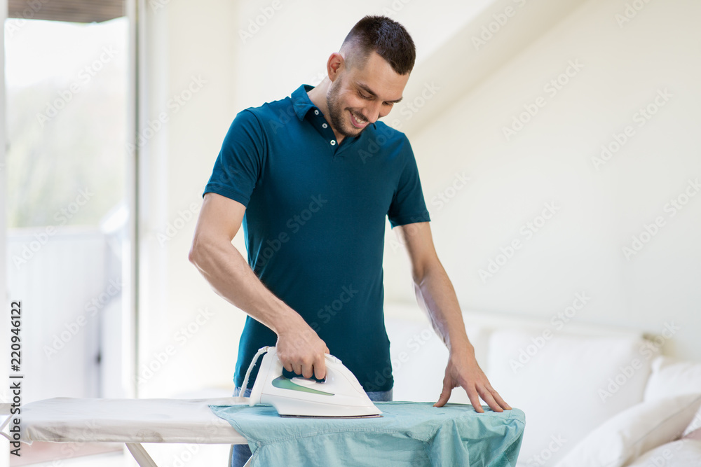 Obraz premium housework and household concept - man ironing shirt on iron board at home